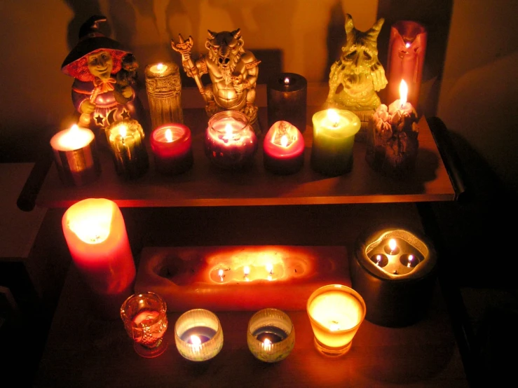 various candles lit on a wooden shelf and surrounded by various statues