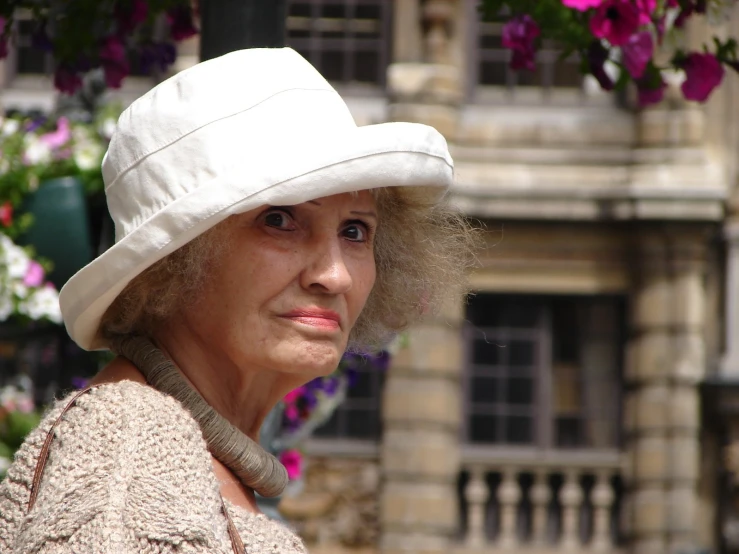 an old woman wearing a white hat stands near a flower garden