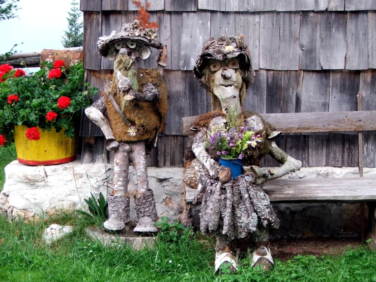 two sculptures sitting on a wooden bench near some potted flowers