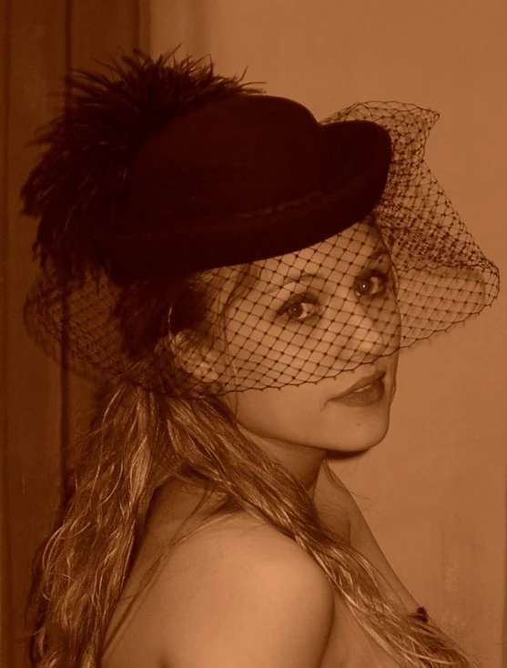 a woman is posing in a hat with netting and feathers