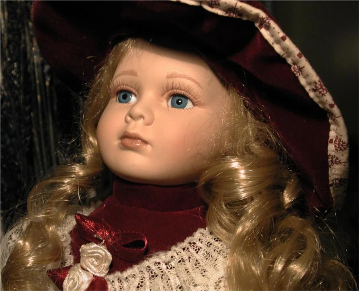 a doll with blonde hair wears a burgundy dress and a bonnet