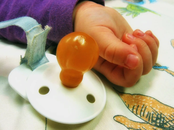 a hand on a toy pacifier with an attached clip