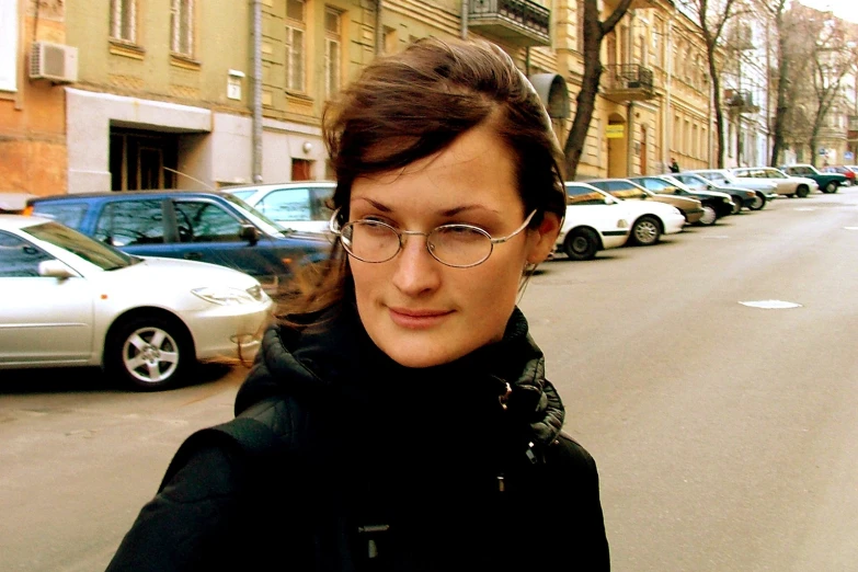 a woman with glasses and coat walking down a street