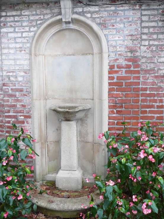 a water fountain and some flowers in front of a brick wall