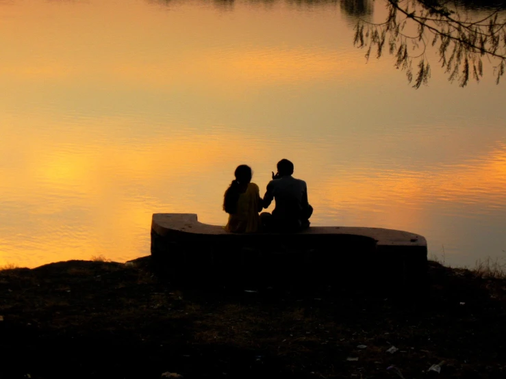 two people sitting on a bench near a body of water