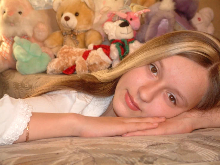 a girl lies on her bed with stuffed animals in the background