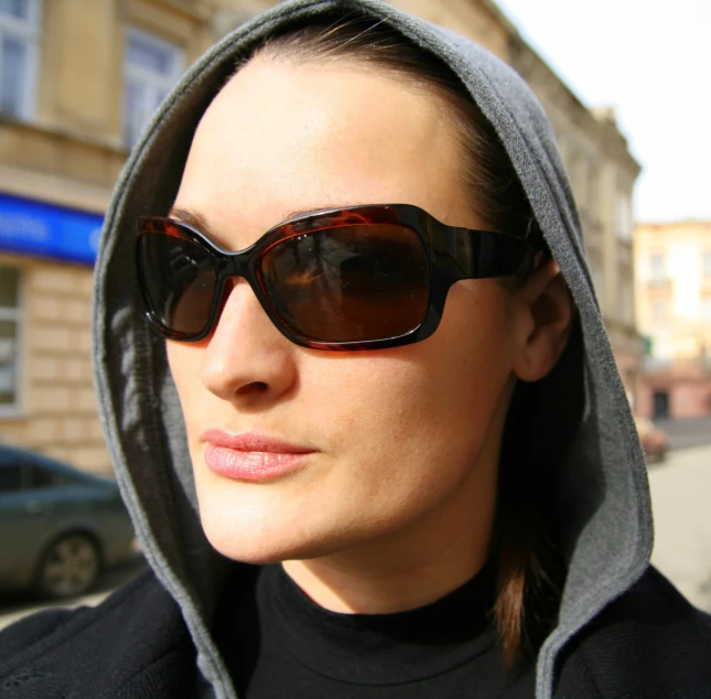 a woman wearing sunglasses and hoodie standing on the street