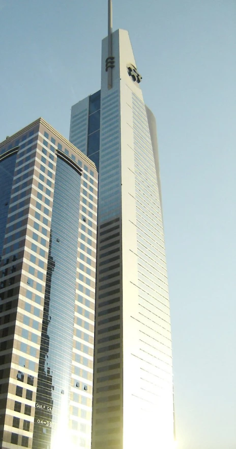 two tall buildings stand near each other in front of the sun