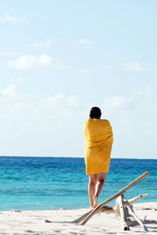 woman wrapped in yellow towel walking towards the ocean