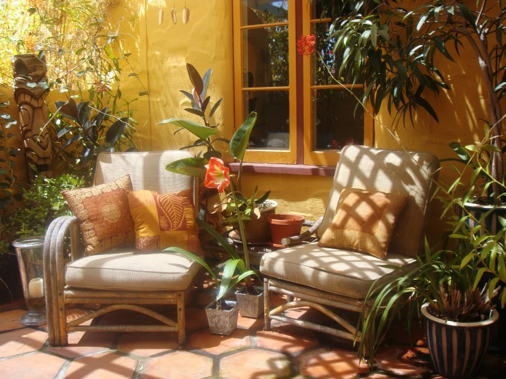 a patio area that contains two chairs, plants, and windows