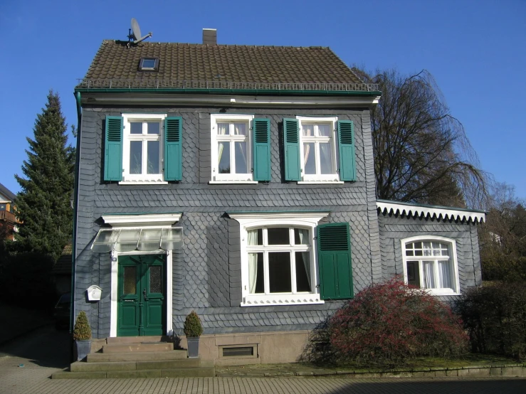 a grey three story house with green shutters