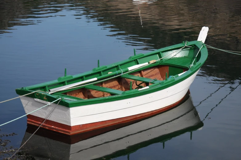 a green boat tied up to a wire on the water