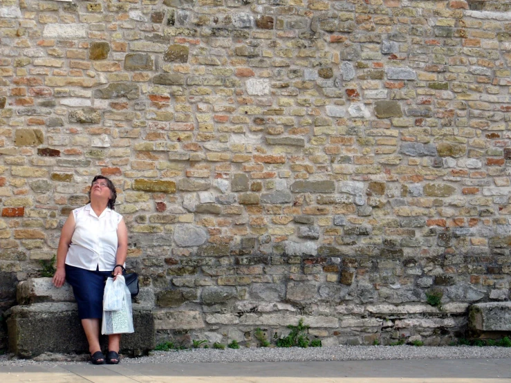 a lady standing against the side of a stone wall