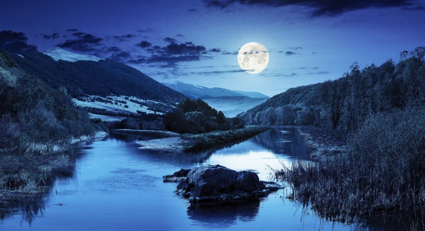 the moon rising over a mountain range reflecting in a river