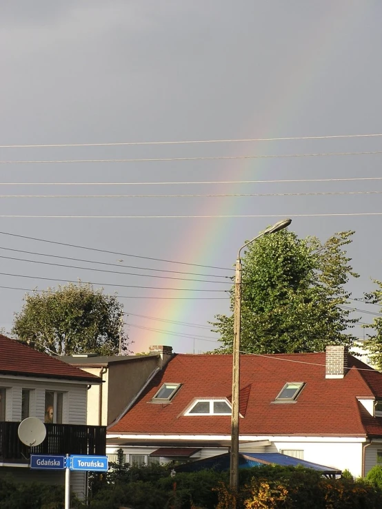 a rainbow shines above some houses near a street sign