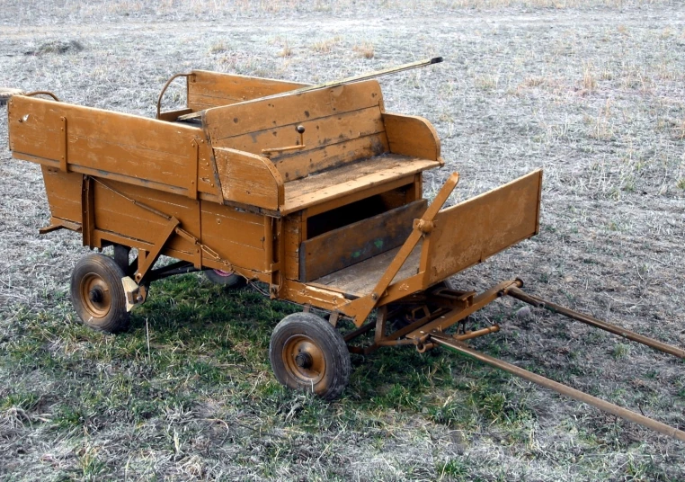 a wooden cart sitting on top of a field next to grass