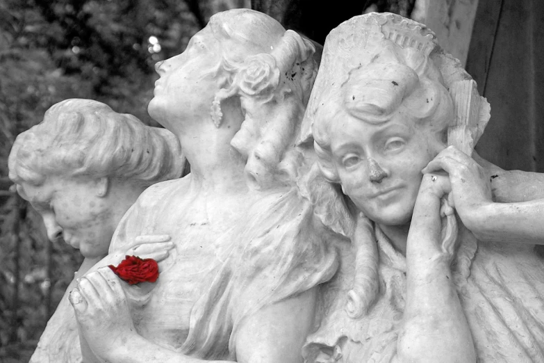 three statues of two women, one holding a piece of red paper