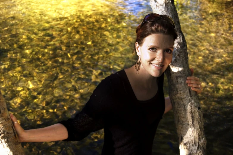 a woman is standing by a tree near a body of water