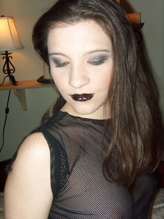 a girl with dark makeup standing in front of a lamp