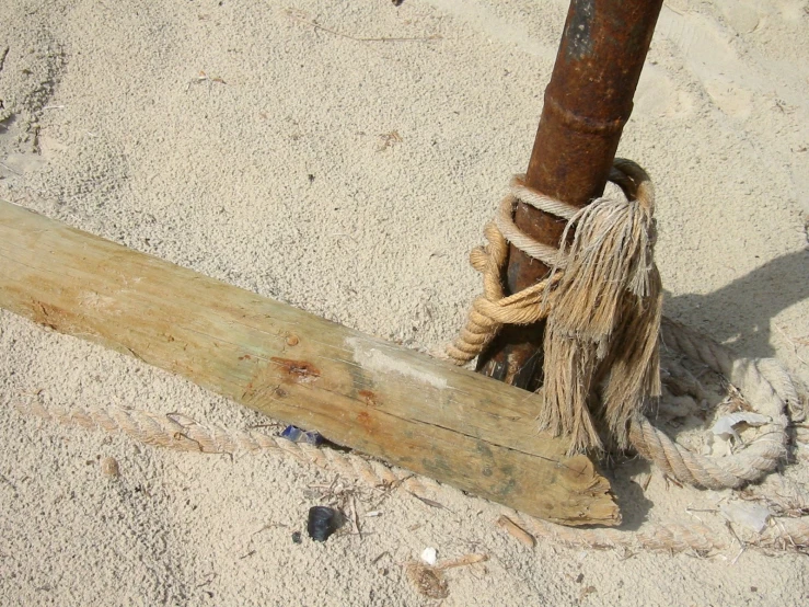 the pole has tasseled rope and is next to a wooden post on the sand