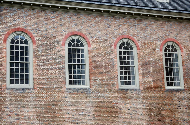 three windows in a brick building with three green benches