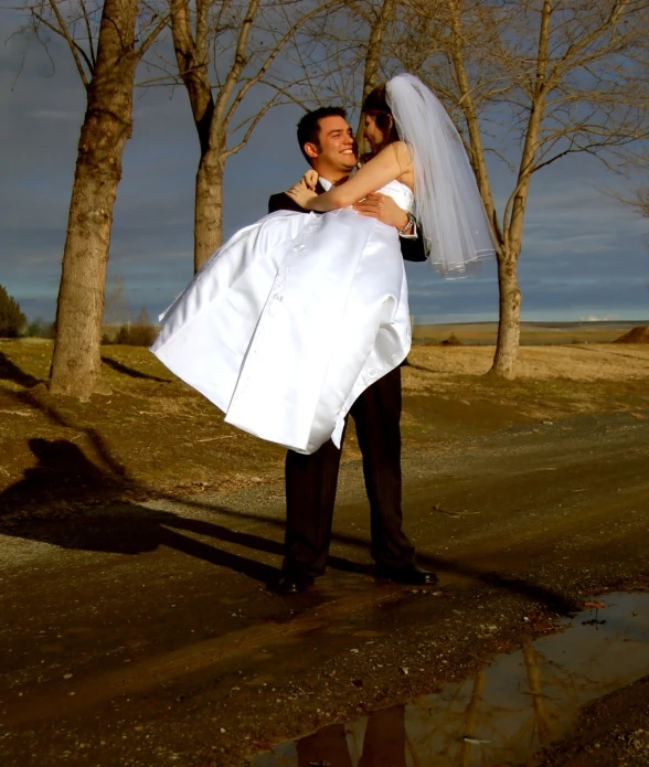 a bride carries a groom in a white dress across a path