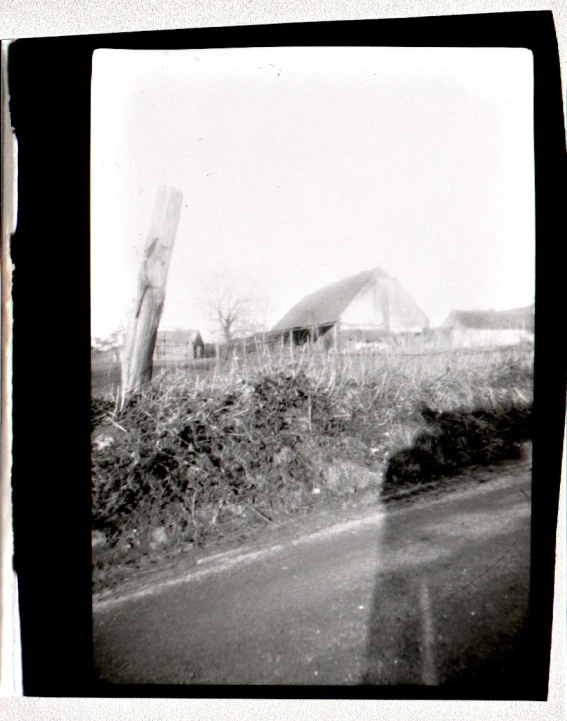 a black and white picture of a barn by the side of the road