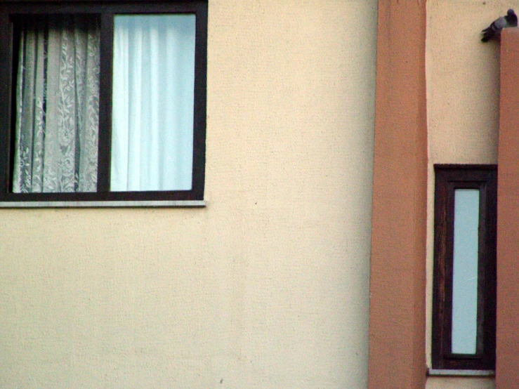 an open window with curtains in between by a wall