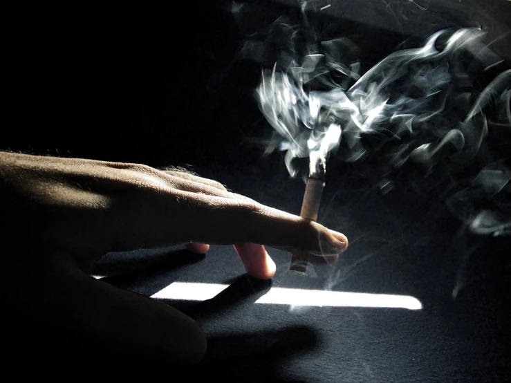 a person's hand holding a cigarette with white smoke coming out