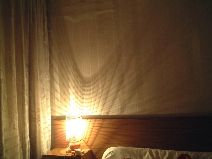 a bed with an open curtain behind it, a lamp on the side table next to it