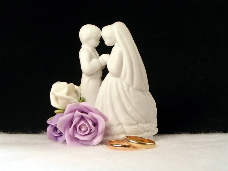 two wedding rings next to a figurine with a flower