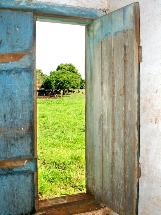 a doorway to a large green pasture next to a dirt field