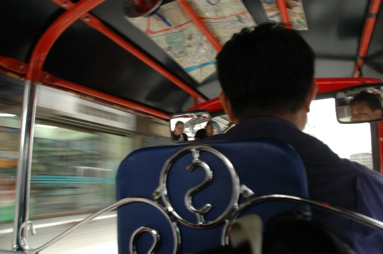 man sitting on seat in a public transit bus with traffic blurry behind him