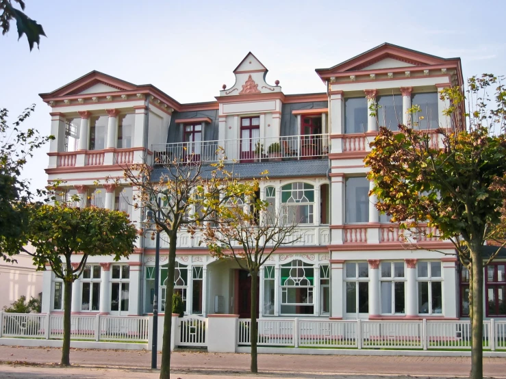 a tall white and pink house with a small red balcony