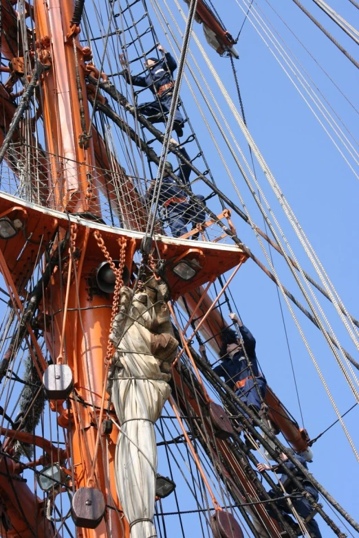 a tall mast with ropes and people climbing them