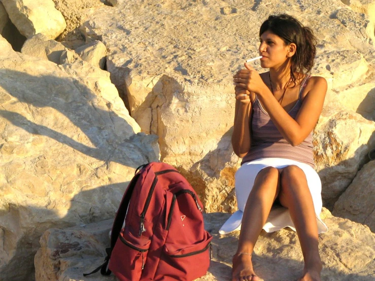 a woman sits on rocks while a backpack holds soing