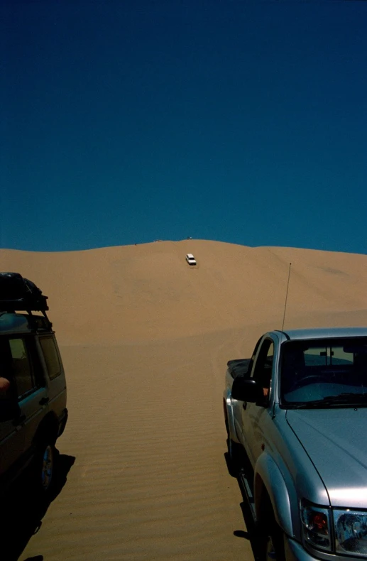 the two cars are parked near the very tall sand dunes