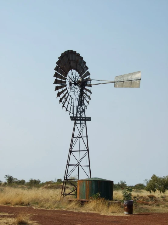 a windmill on a dirt field near a large tank
