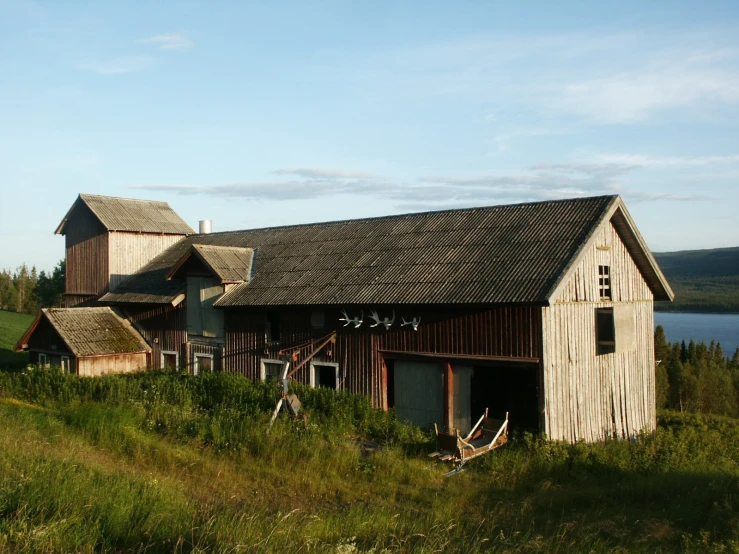 a barn stands alone in the grass by the water