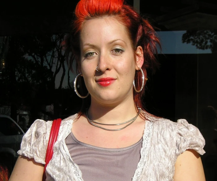 a girl with red hair and piercings stands in the shade