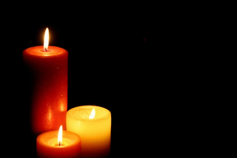 three lit candles are on a black surface