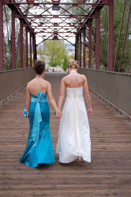 two women in dresses walk along a bridge