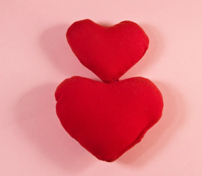 two heart shaped red objects against a pink background