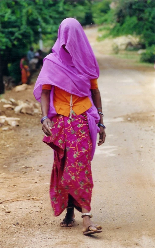 a woman wearing a purple sari walks down the road