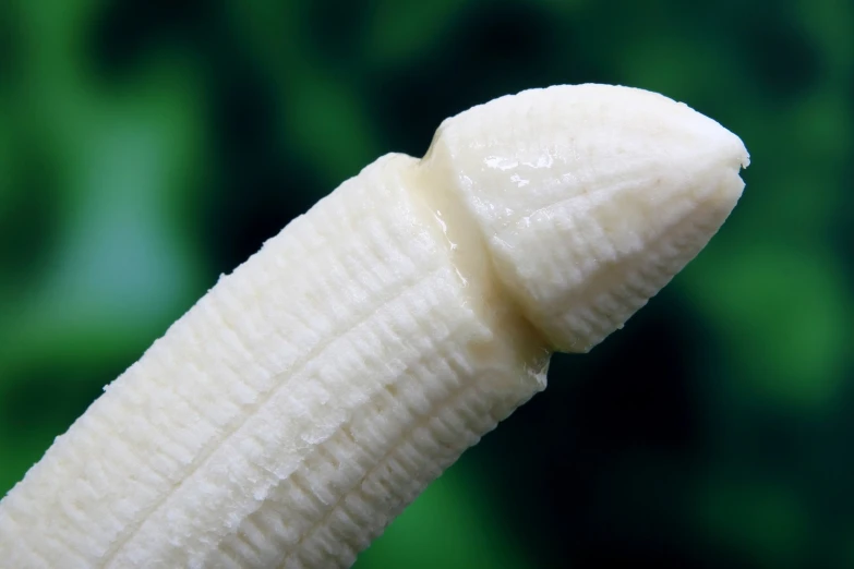 the peeled banana is held up against a green background