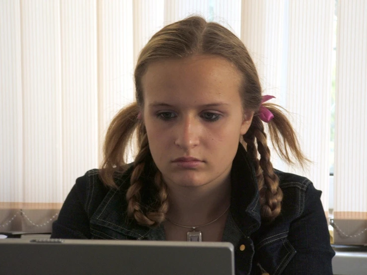 a  with a ponytail on is staring at her computer