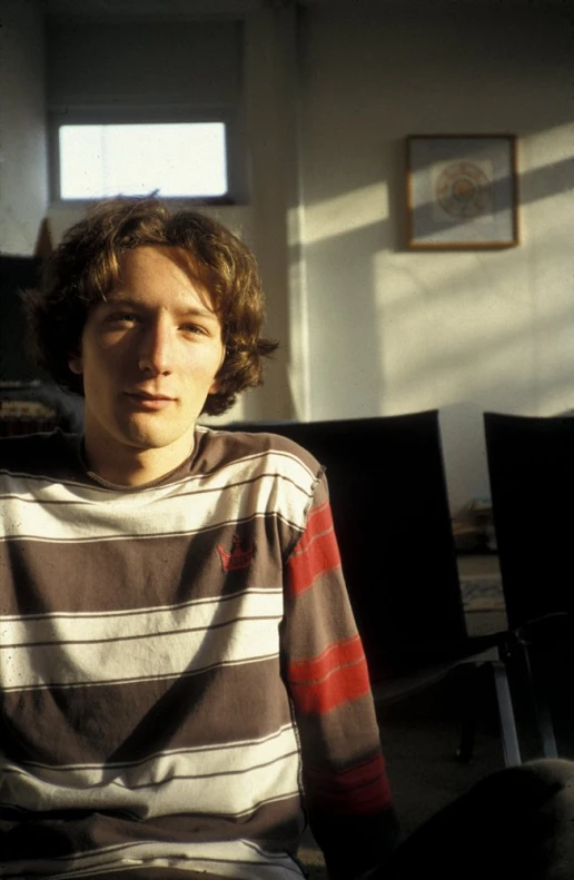 a young man posing for the camera while he is sitting on a chair