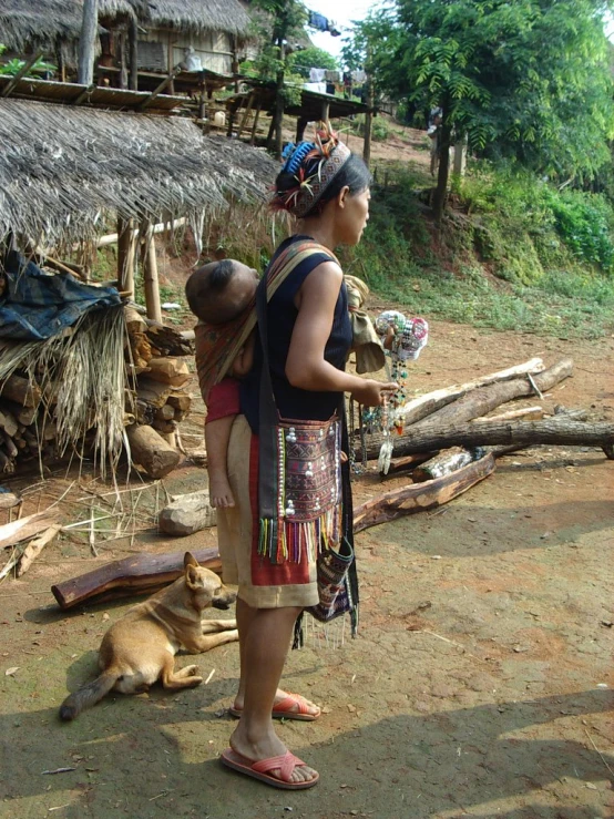 there is a woman with a child in her sling next to a dog