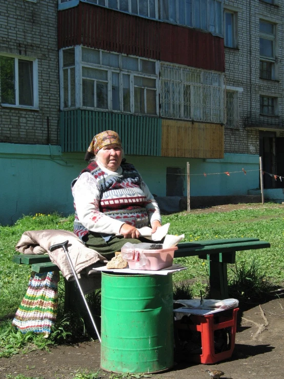 a women sitting on top of a table over a green trash bin