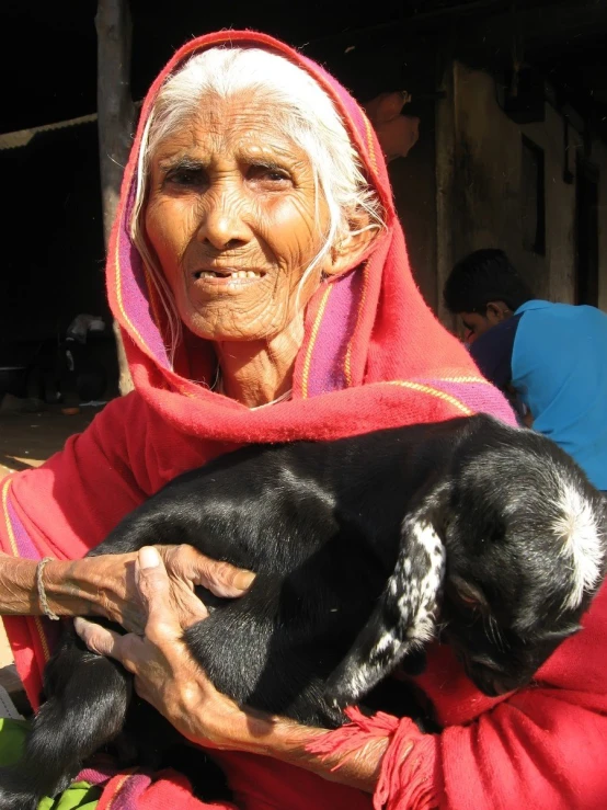 an old woman wearing a red hoodie holds a black and white dog